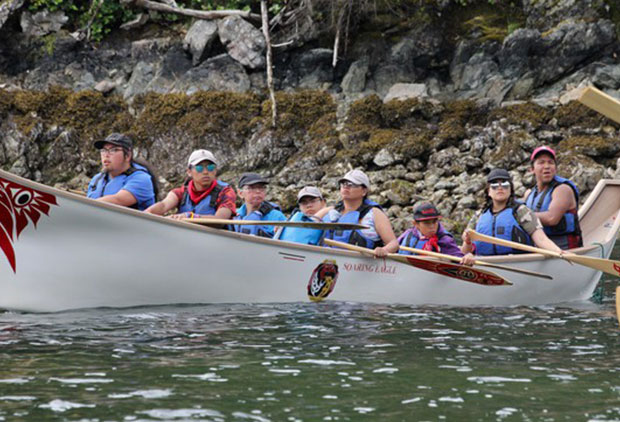 People wearing lifejackets paddle through the water in a large canoe.