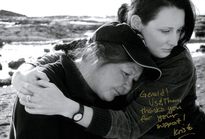 A black-and-white shot from the documentary Us and Them. A woman holds another in an embrace.